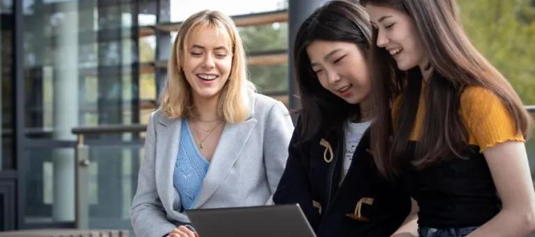 Three students sat looking at one laptop screen